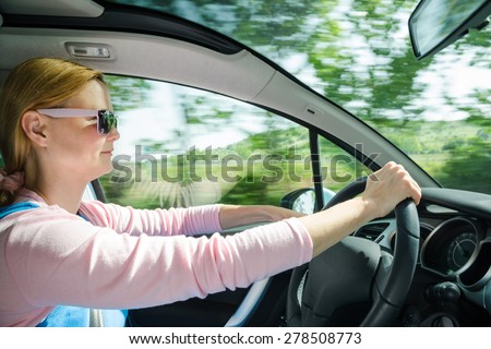 Smiling beautiful woman in sunglasses driving at high speed car with panoramic windshield. Internal stock photo with low shutter speed and blurred in motion natural background.