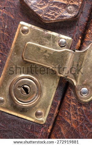 the closed metal rusty lock closeup on part of an old suitcase with the textured leather surface of dark brown color