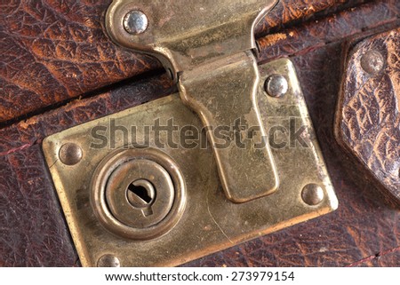 the closed metal rusty lock closeup on part of an old suitcase with the textured leather surface of dark brown color