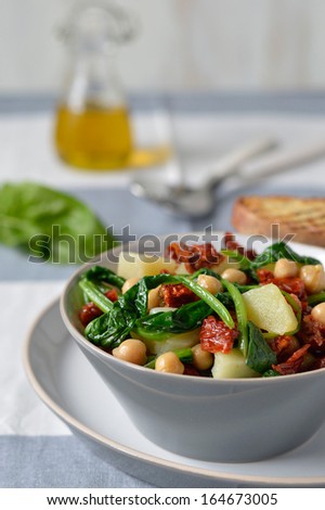 Light salad with spinach, chickpeas and potatoes with a salad bowl on the cloth surface with cutlery and bread toasts (bruschette). Italian food.