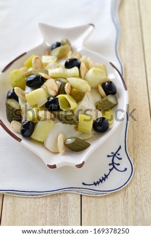 Warm Salad with dried cod, leek, almonds on a plate in the shape of a fish on a light wooden background. Italian food.