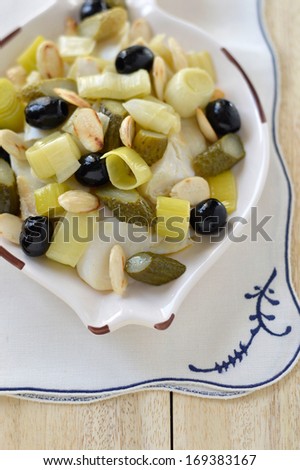 Warm Salad with dried cod, leek, almonds on a plate in the shape of a fish on a light wooden background. Italian food.