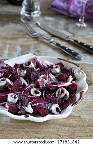 Marinated anchovies, radicchio lettuce and beets in a salad bowl in the shape of a shell on a wooden background.