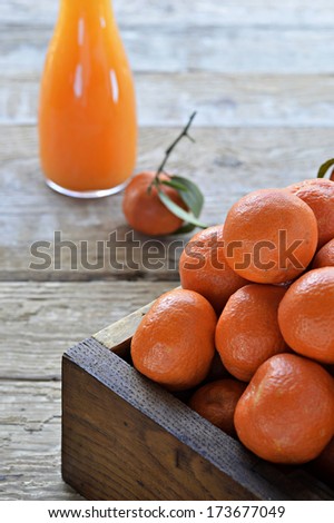 Whole tangerines (clementines) with green leaves in a wooden box. Freshly squeezed tangerine juice in a carafe. Close up.