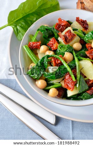 Salad light with spinach, chickpeas and potatoes with a salad bowl on the cloth surface with cutlery and bread toasts (bruschetta). Italian food.