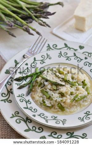 Green asparagus risotto on a plate with green ornament, decorated: fresh green asparagus and Parmesan cheese.
