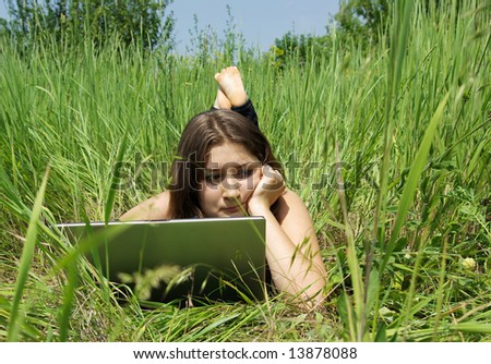 The girl works on a computer on a green grass
