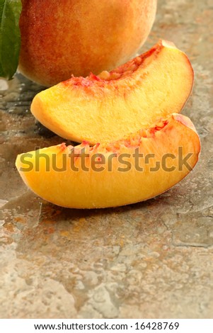 Whole and sliced fresh picked peach on a stone counter.