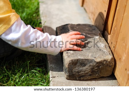 Toddler trying to move a heavy stone outside in the sunshine in summer