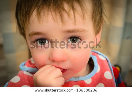 Beautiful Toddler looking into the camera biting fingers