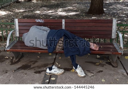 BUCHAREST, ROMANIA- JULY 01: Homeless man sleeps on the bench in a public park on July 01, 2013 in Bucharest, Romania. Bucharest has almost 5000 homeless men in 2012.
