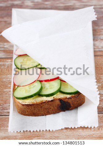 Sandwich with fresh vegetables (radish, cucumber) in  white paper bag