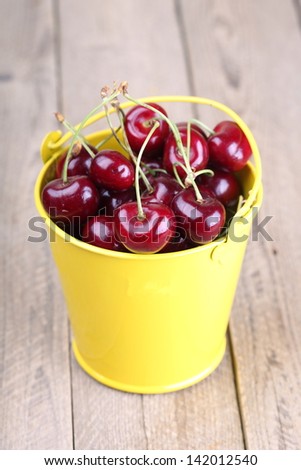 Ripe cherries in a yellow bucket on a wooden background