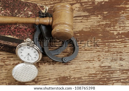 Judge\'s gavel, handcuffs, legal book and watch on old wooden background