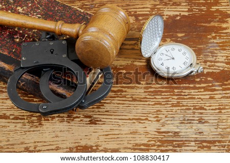 Judge\'s gavel, handcuffs, legal book and watch on old wooden background