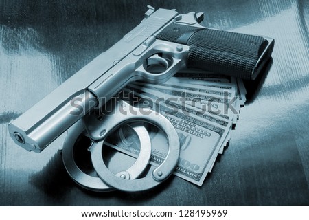 Stack of money, gun and handcuffs on table