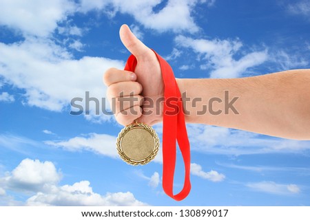 Hand holding gold medal on sky background