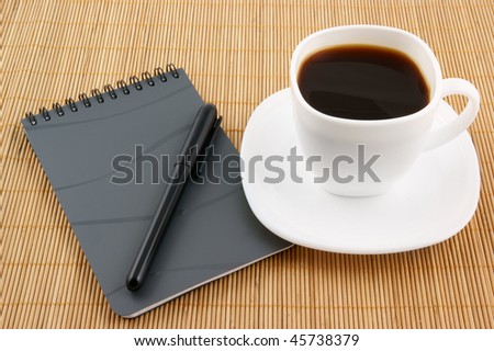 Pen on a black spiral squared notebook with cup of coffee