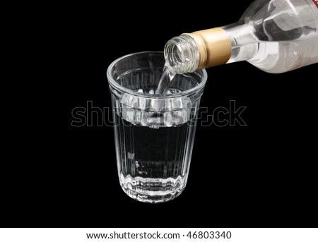 Vodka from the bottle is poured into a glass isolated on black