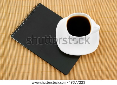 Black spiral squared notebook with cup of coffee