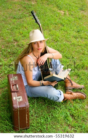 Young woman with guitar and suitcase on grass