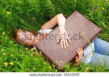 Woman smiling with suitcase in green grass as vacation symbol