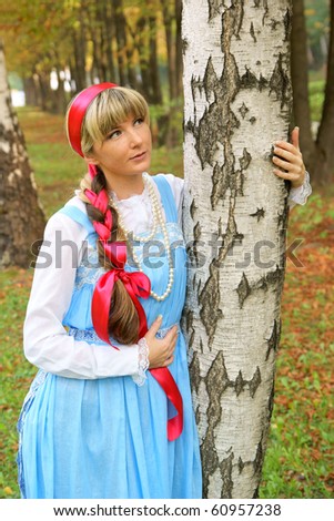 Young woman in folk russian dress near birch