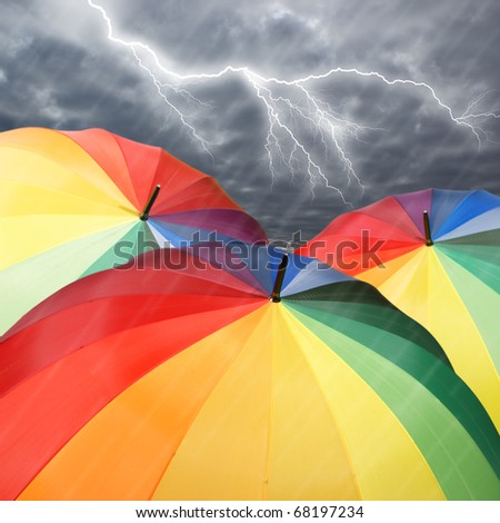 Rainbow umbrellas on dramatic sky background under rain