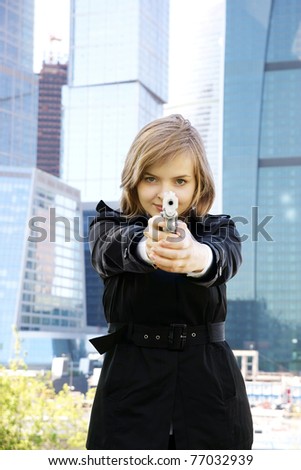 Young beautiful woman with gun on city background