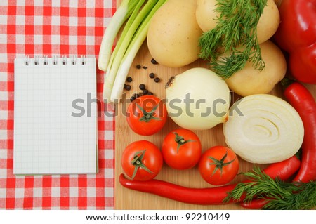 Notebook and cutting board with vegetables on tablecloth