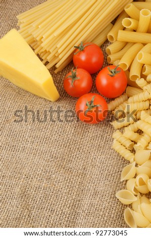 Raw macaroni with tomatoes and cheese on burlap background