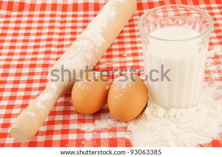 Flour, milk, eggs and rolling pin on red checked tablecloth