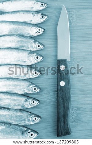 Bleak fish and knife on wooden background in blue tone