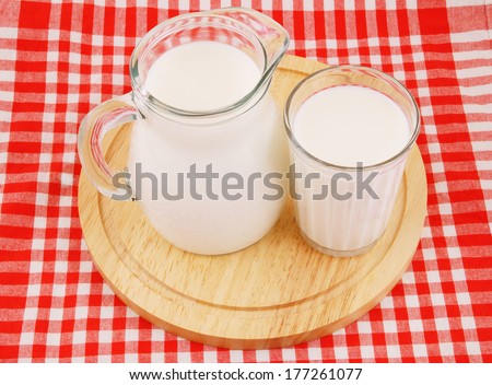 Milk in pitcher and glass with wooden board on red tablecloth