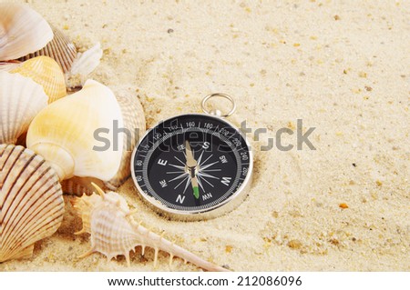 Seashells with compass on sand background, travel concept