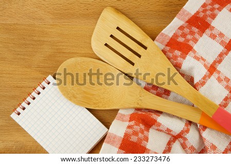 Tablecloth, spatula, notebook and spoon on wooden table background