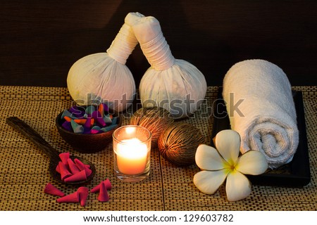 Thai spa massage setting with herbal compress balls, towel, frangipani, candle and incense cone