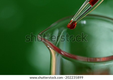 Pipette adding red fluid to beaker on green background