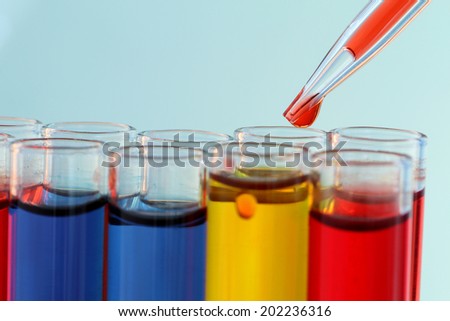 Pipette adding red fluid to test tubes on blue background