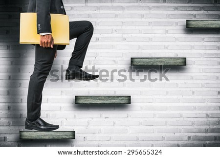 businessman holding files climbing stairs on brick wall
