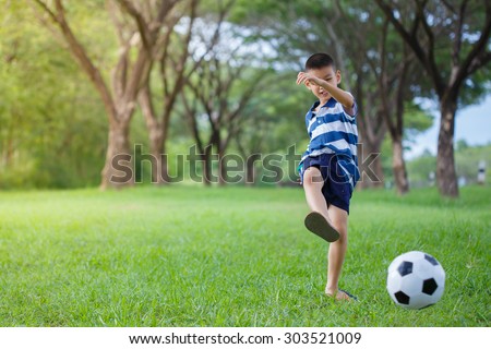 asian kid playing soccer in the park, Authentic action kicking ball