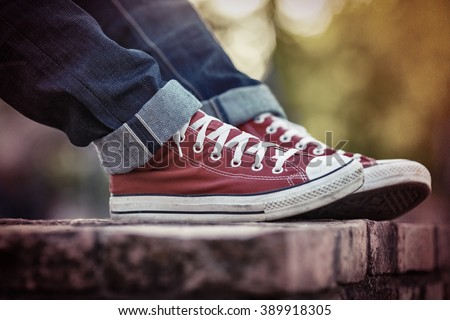 closeup of legs wearing blue jeans and red sneakers againt sun light