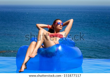 Beautiful young woman sitting on inflatable chair sunbathing. Relax in swimming pool with wonderful sea views.
