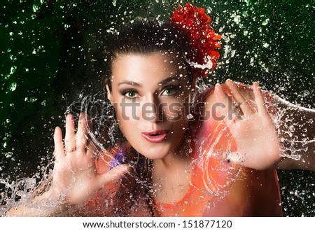 Happy party girl. Close up pretty young woman with floral hair accessories and orange clothing on off black background with abstract water splashes.