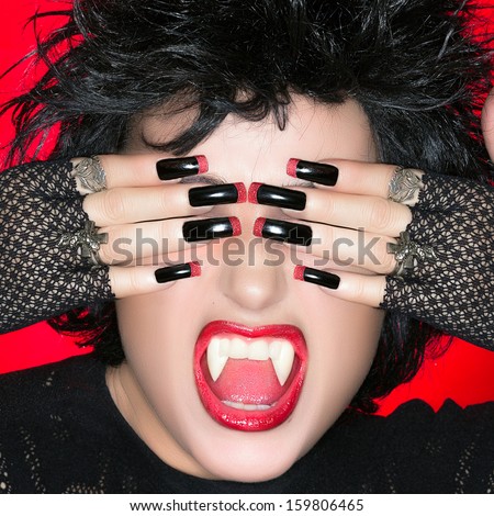 Halloween vampire. Beautiful young woman screaming with big fangs and luxury nails in black and red