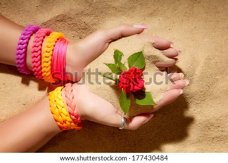 Closeup of hands with fluorescent bracelets catching a rose from the sand. Ecologist girl. Colorful summer complements.