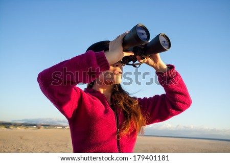 Ecologist young woman watching the environment birds on the coast with binoculars. Wide angle of view