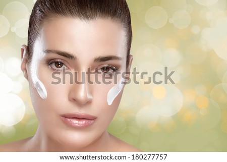 Gorgeous young woman having a spa beauty treatment with cream to her clean face in a skincare and therapy concept, closeup of her face on green background