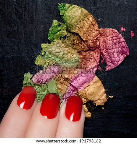Fingers with red nails and colorful crushed eye shadow on black stone. Manicure and makeup concept. Closeup image isolated on black