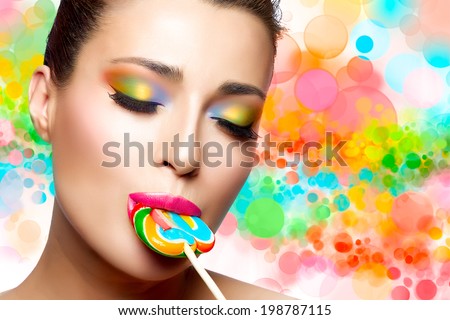 Sweet kiss. Candy girl. Close up portrait of gorgeous young woman with light makeup, looking at the camera with colored sweet candy on her sexy pink lips. Colorful background.